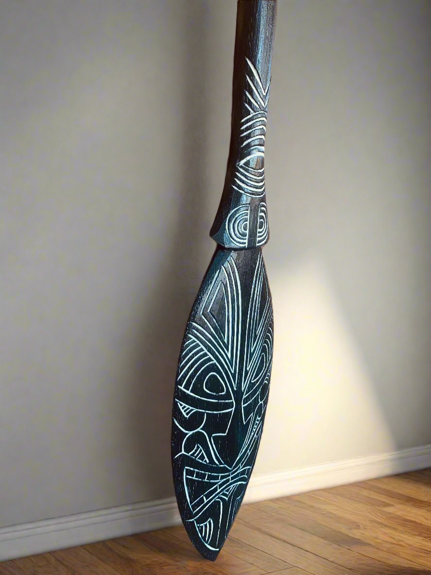 Dark wooden paddle with white geometric tribal carvings leaning against a wall