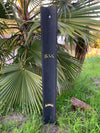 Tall dark wooden post with rectangular and arched cutouts in a garden with palm leaves