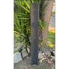 Dark vertical wooden post with scalloped top in a garden beside rocks and a tree.