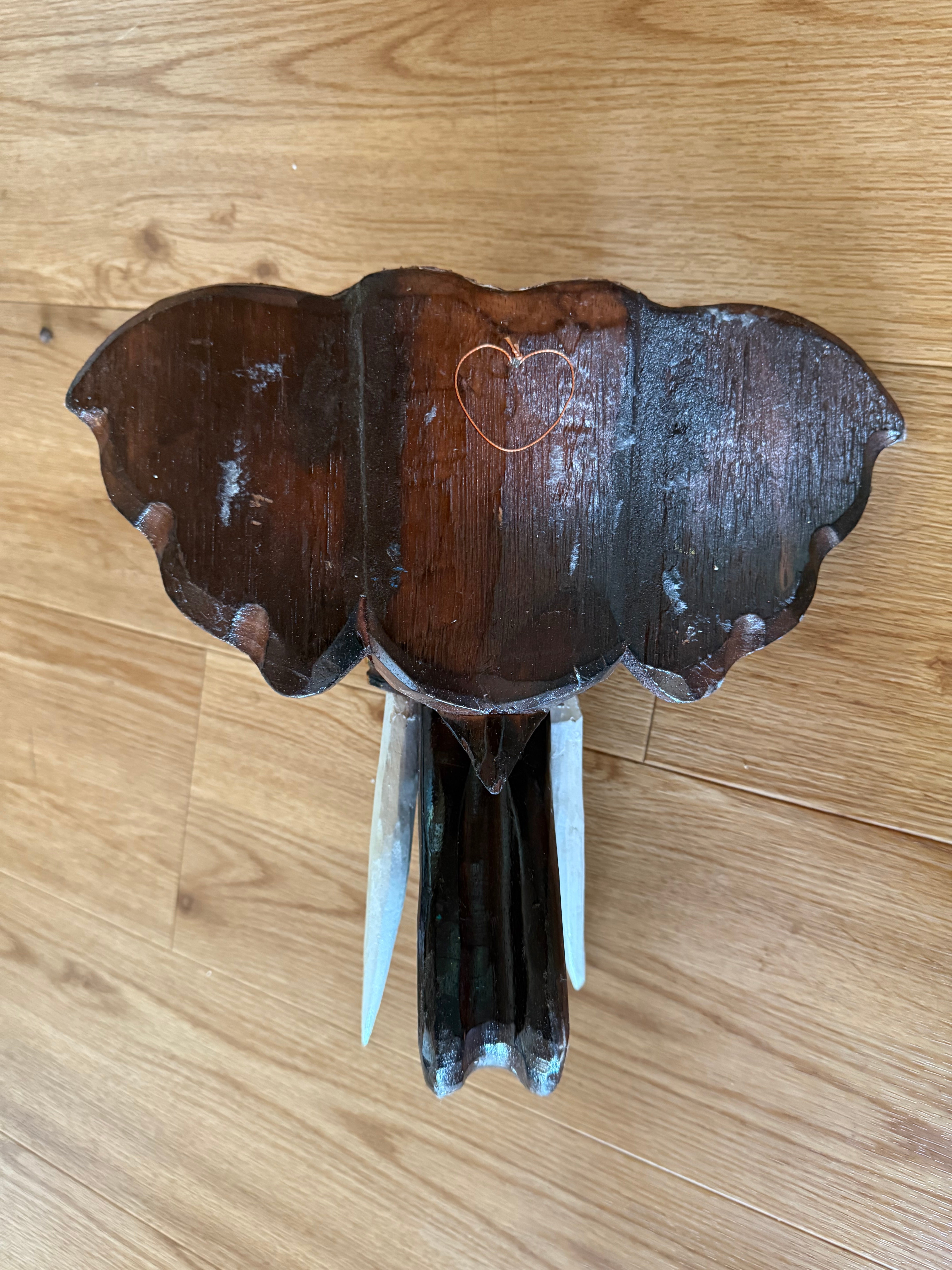 Dark wooden wall decor with scalloped edge, copper heart outline, and white tusk-like protrusions.