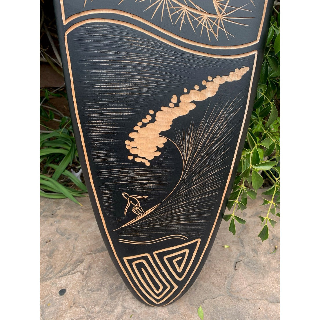 decorative black surfboard with copper etching of a surfer riding a wave and geometric motifs