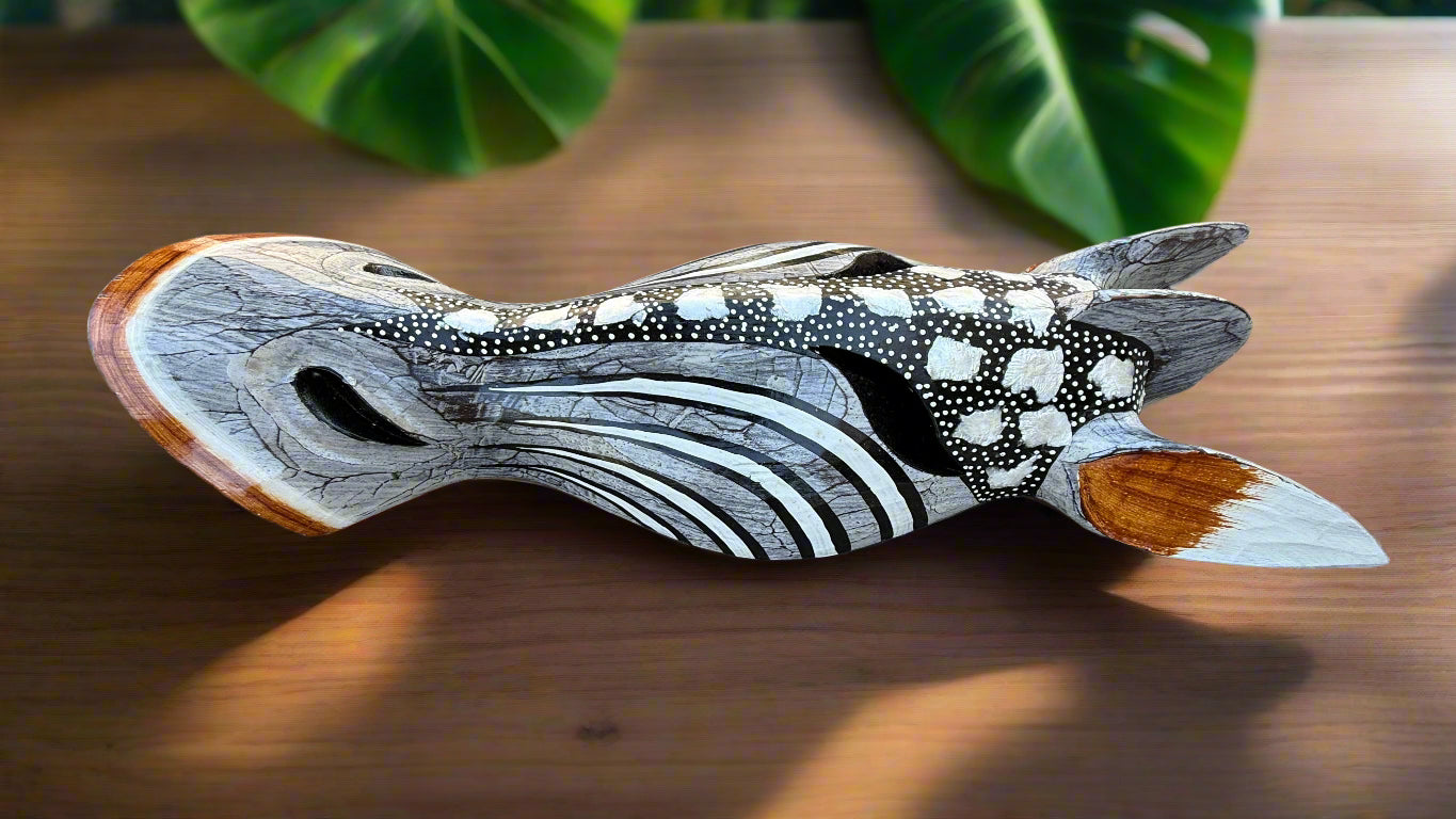 Carved wooden fish sculpture with black and white dot and stripe patterns on a wooden table.