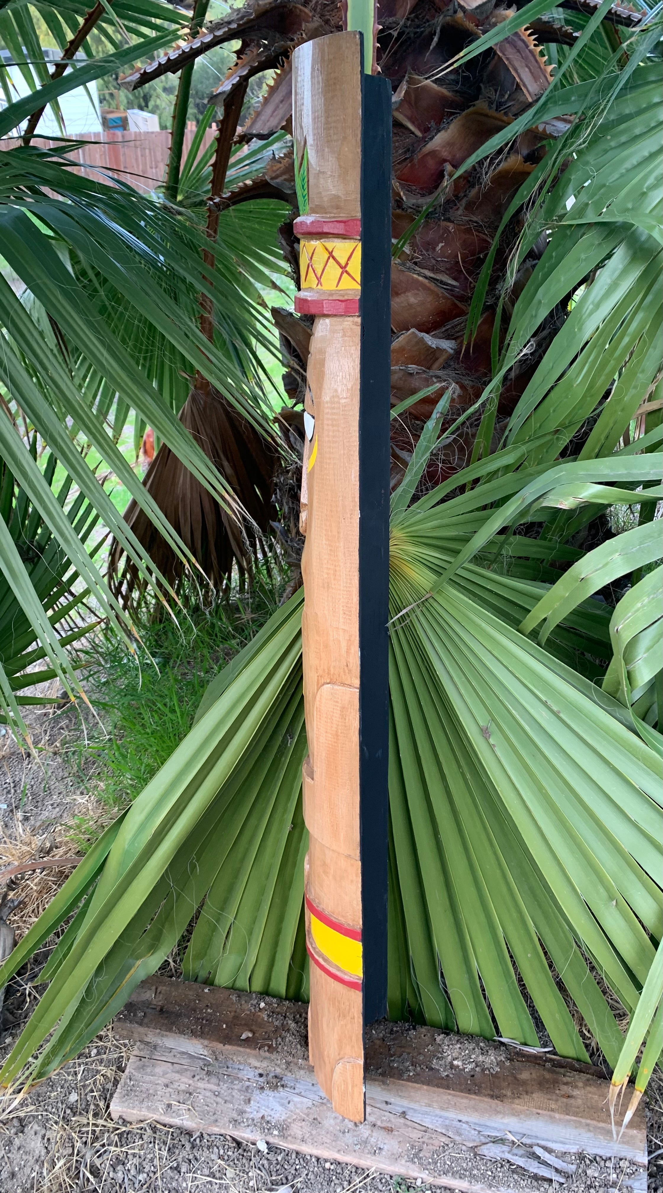 Decorative carved wooden post with yellow and red geometric bands beside palm leaves