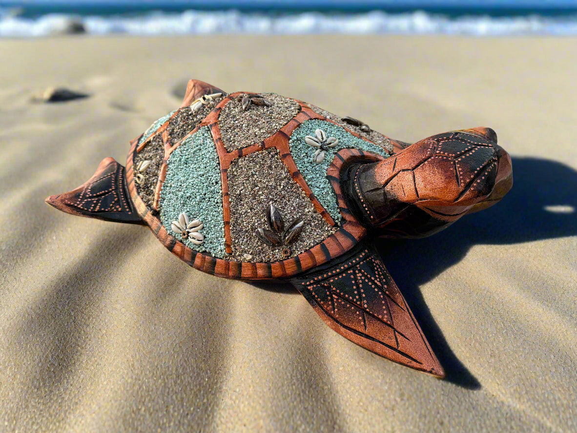 decorative mosaic sea turtle sculpture on sandy beach with ocean in the background