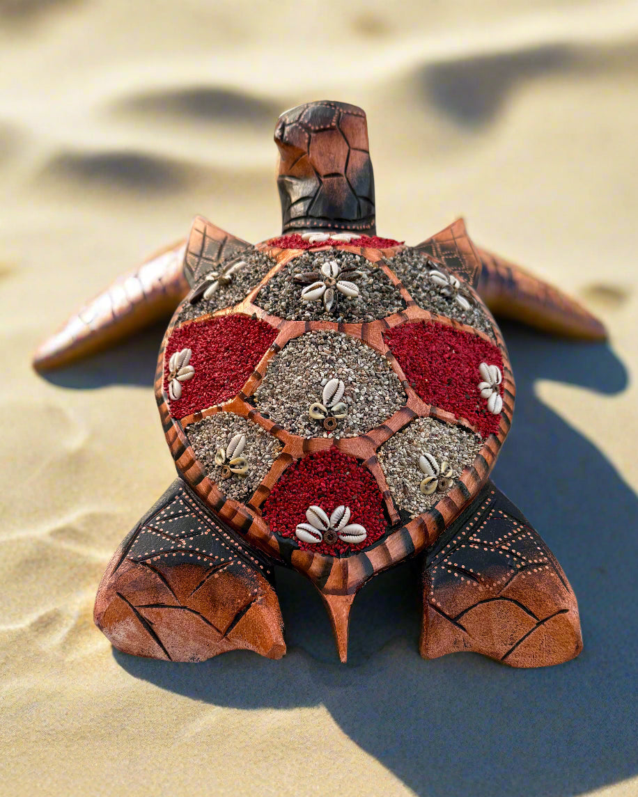 Decorative mosaic sea turtle sculpture with red and gray shell panels on sandy beach