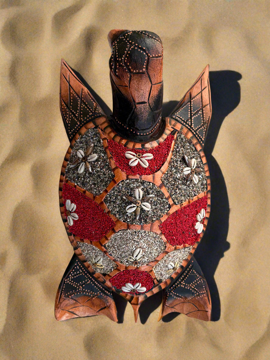 decorative mosaic turtle sculpture with shell made of red and gray stones and cowrie shells on sand