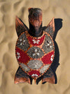 decorative mosaic turtle sculpture with shell made of red and gray stones and cowrie shells on sand
