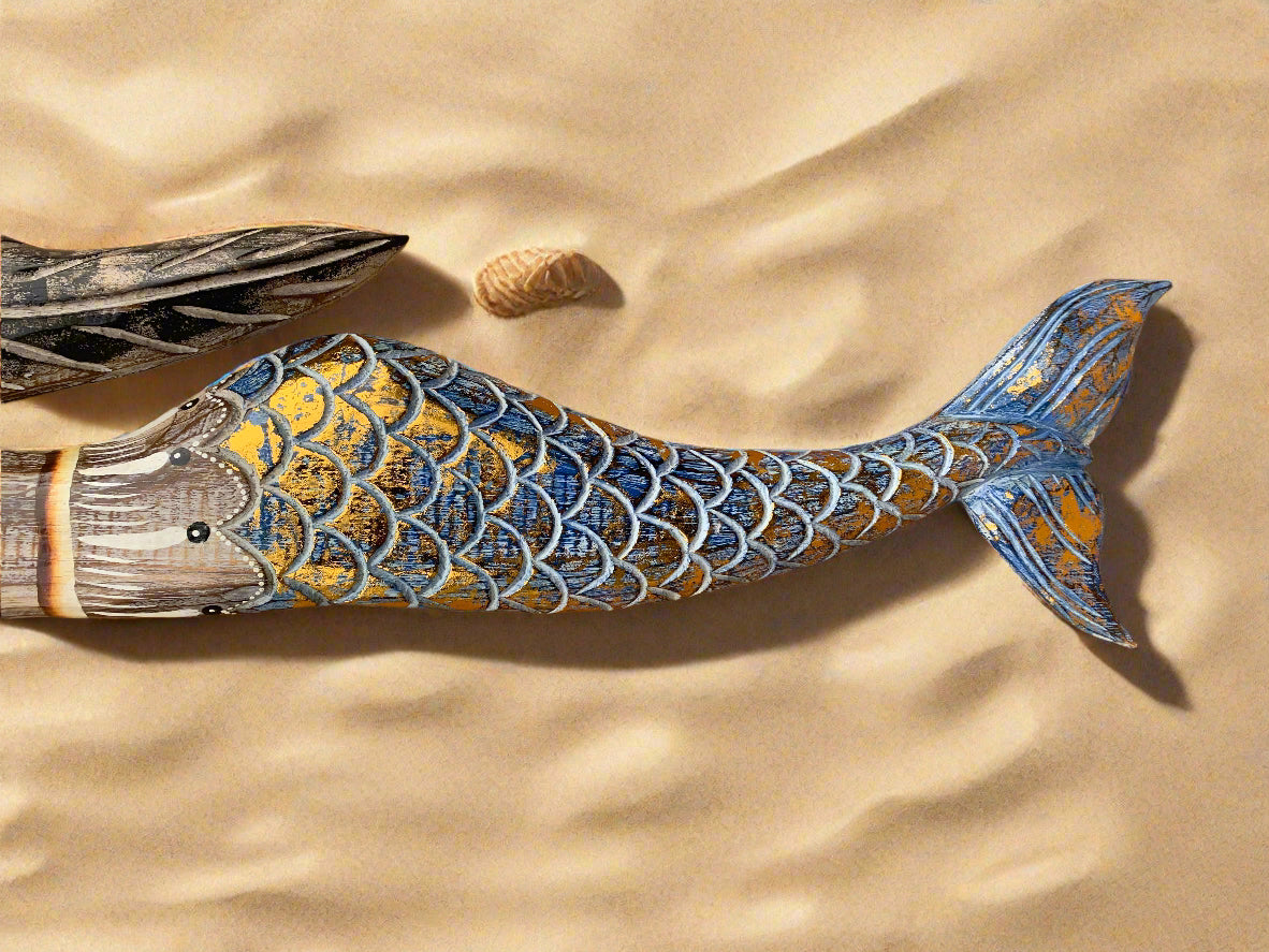 hand-painted wooden fish statue with blue and gold scales on sand background