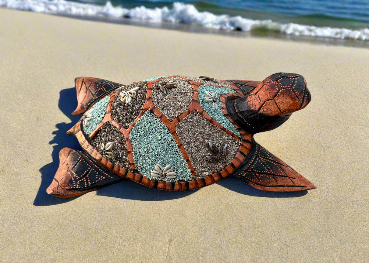 Decorative tiled sea turtle sculpture on the sandy beach with ocean waves in the background.