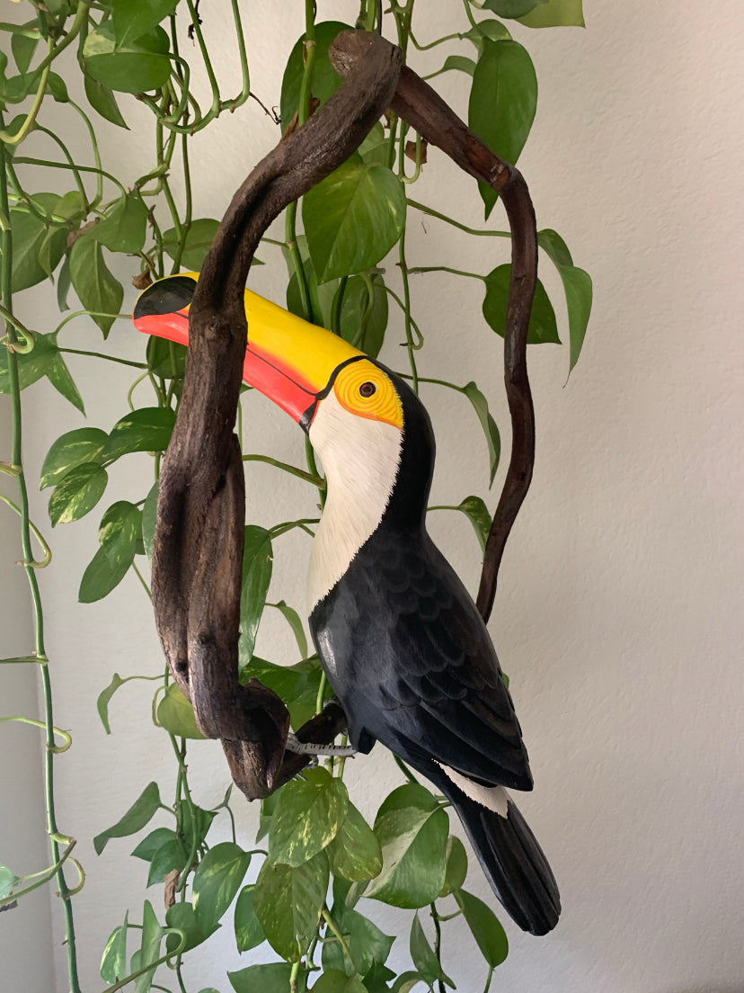 decorative toucan statue with bright yellow beak perched on a branch among green vines