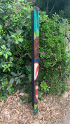 Outdoor decorative wooden totem pole with teal and red carved patterns leaning against shrubs
