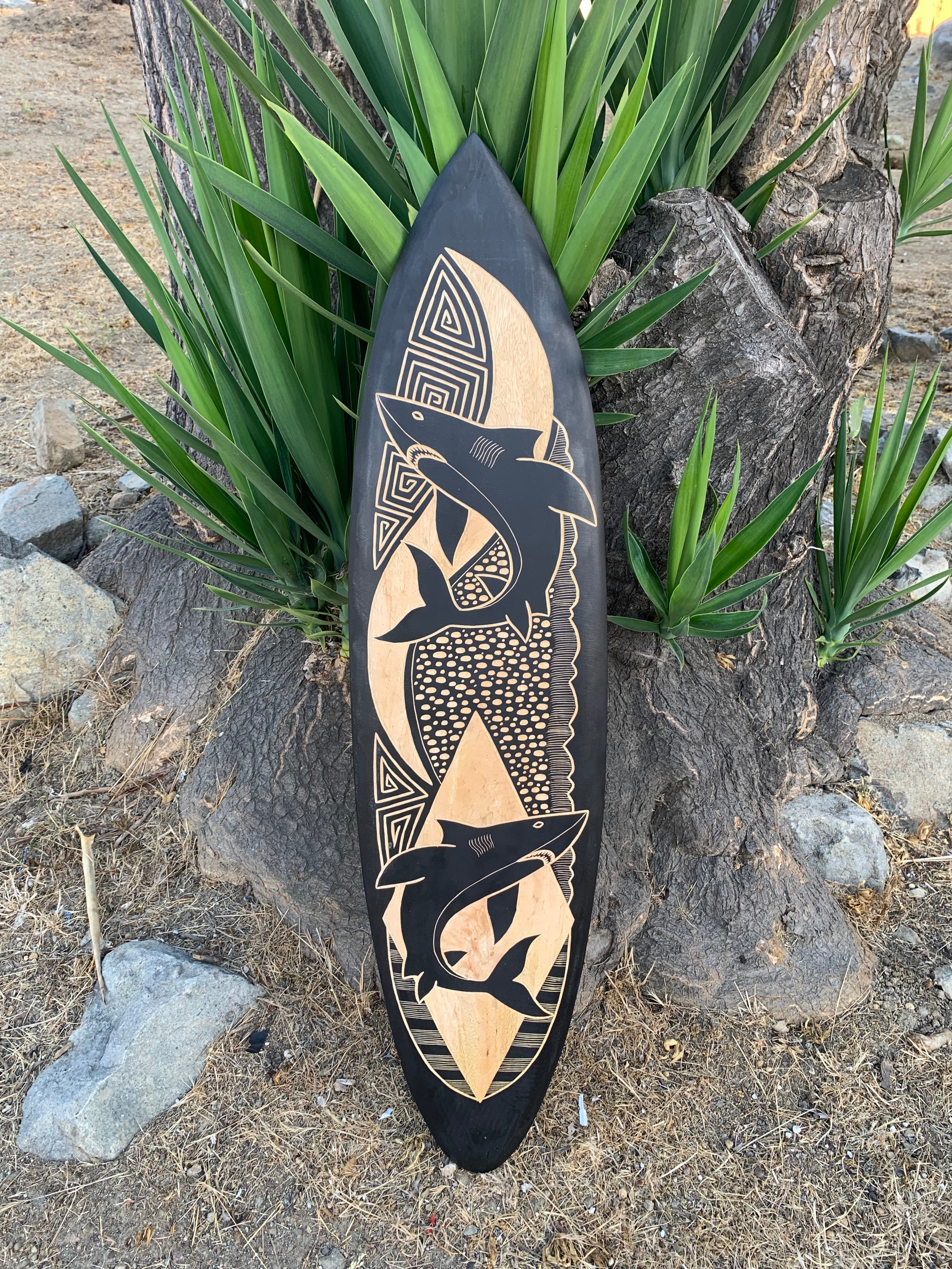 Black wooden surfboard wall art with tan dolphins and geometric patterns