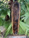 long dark dugout canoe with rope-wrapped edges hanging among palm leaves