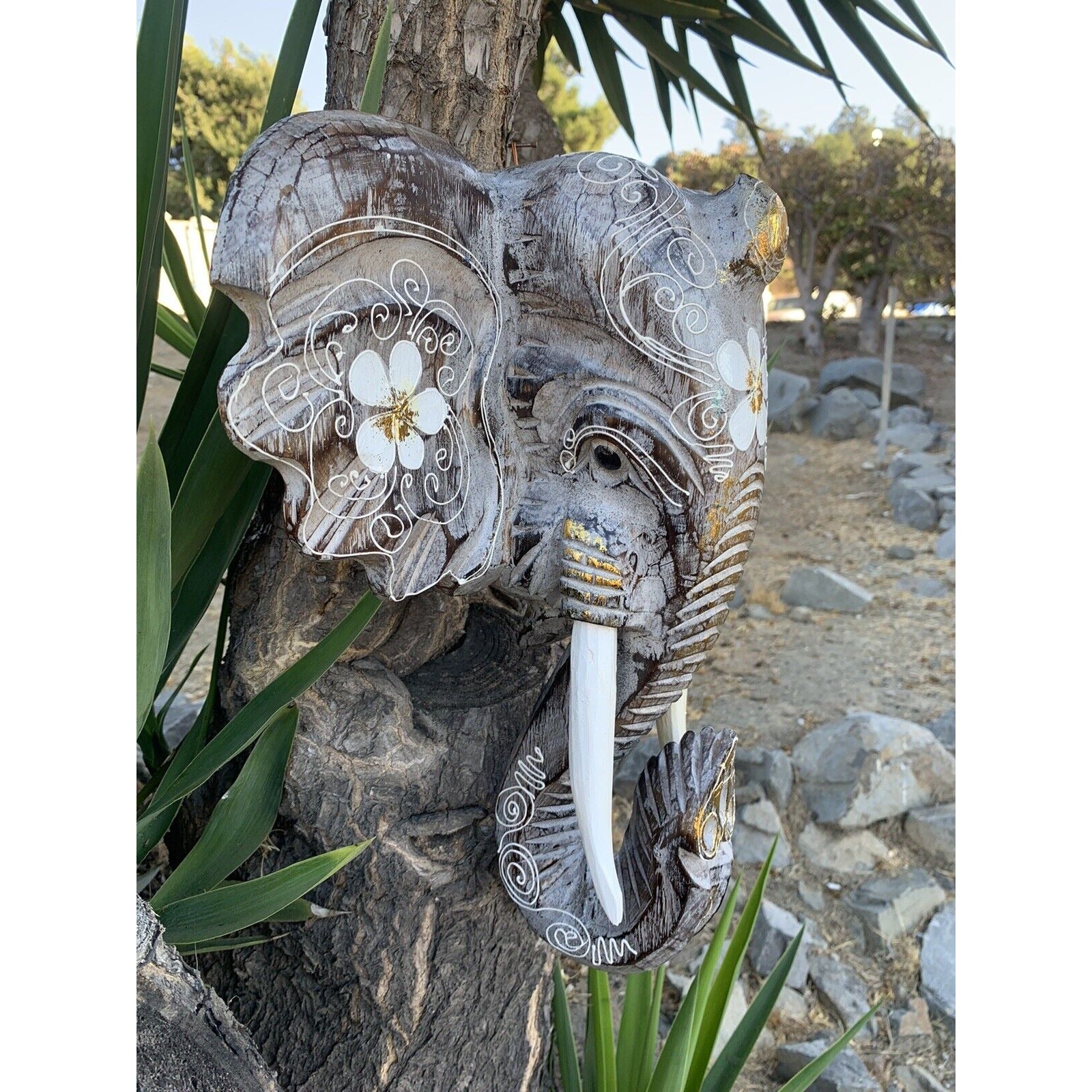 Carved elephant head on a tree with white floral ornamental patterns.