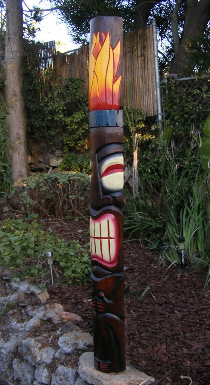 Colorful carved totem pole with flame design on top standing in a garden