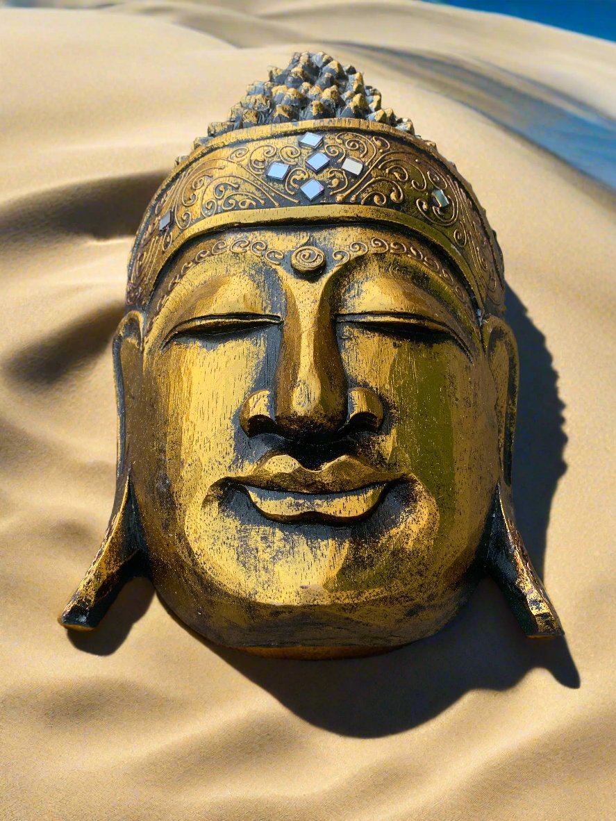 golden Buddha head statue with ornate crown resting on sandy dunes