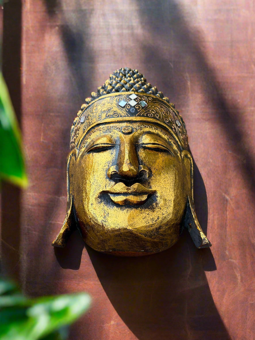 golden buddha head statue with ornate crown on a rust-colored wall