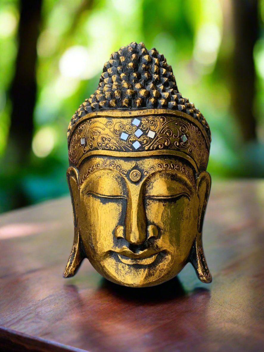 Golden Buddha head statue with ornate jeweled headband, outdoors in greenery.