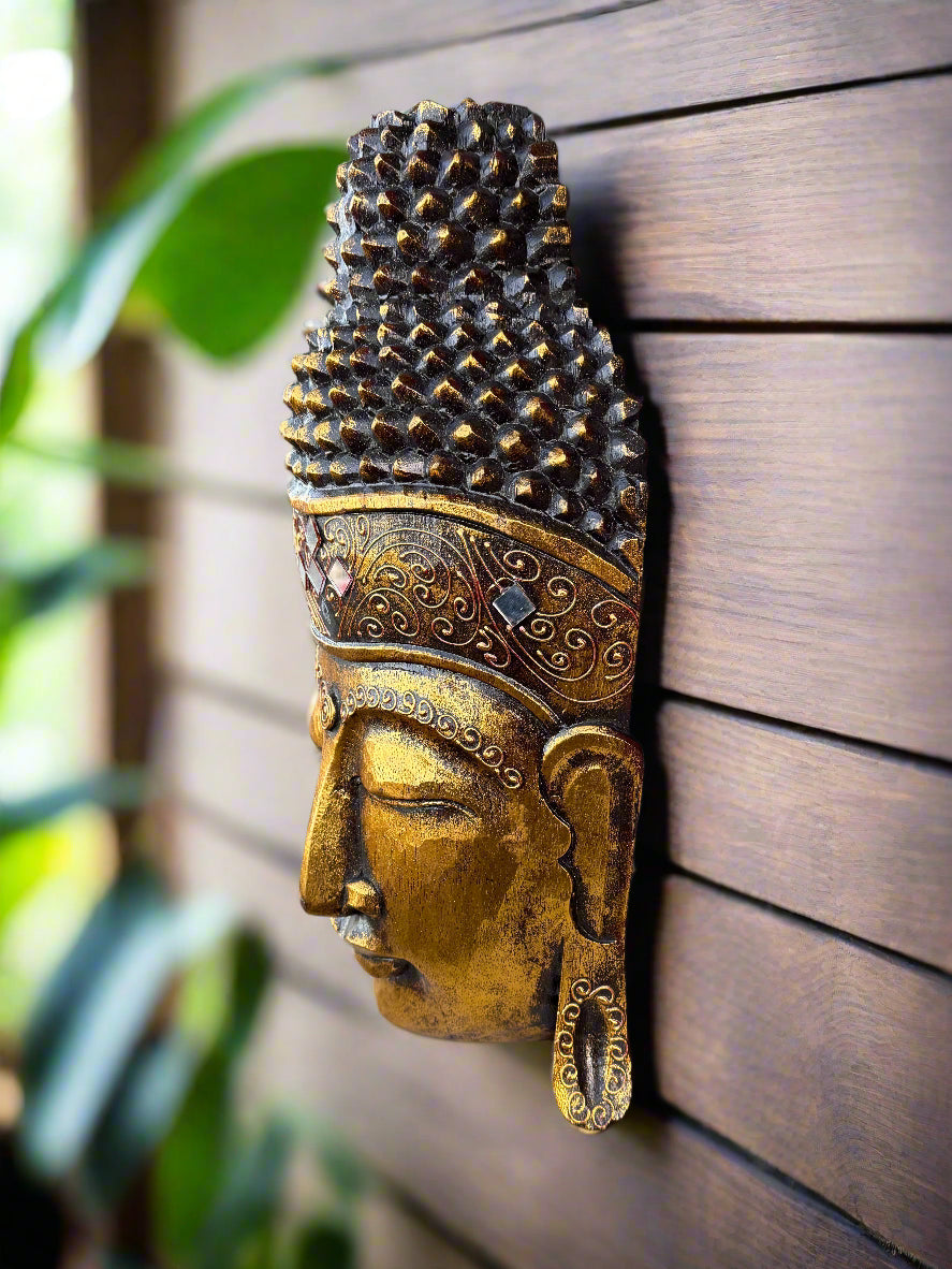 Golden Buddha head wall sculpture with ornate crown and textured hair against a wooden background