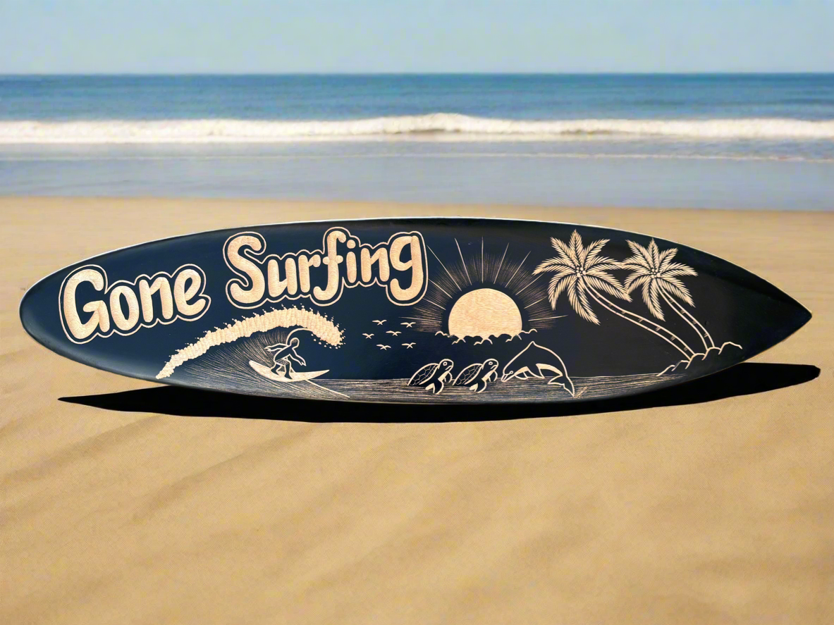 Surfboard with 'Gone Surfing' graphic on a sandy beach by the ocean.