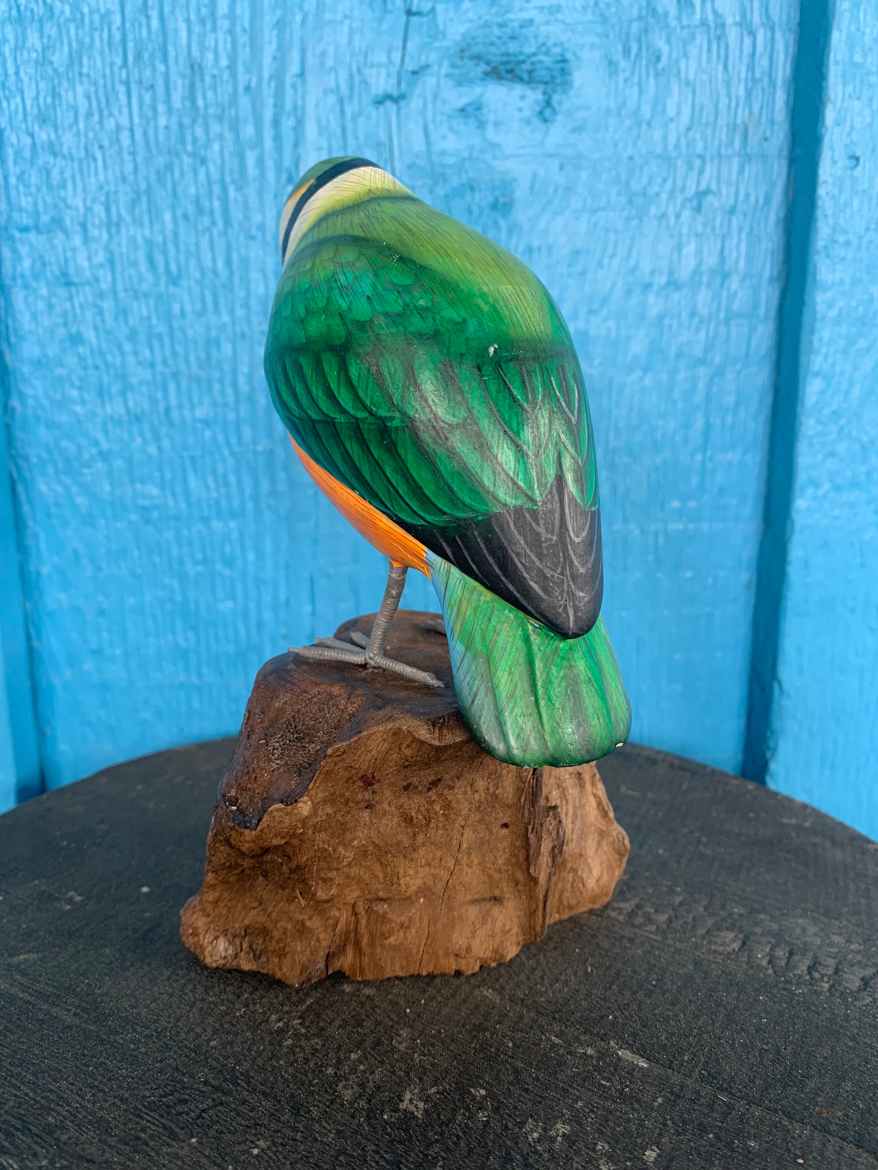green carved wooden parrot statue perched on a rock against a blue wooden background