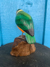green carved wooden parrot statue perched on a rock against a blue wooden background