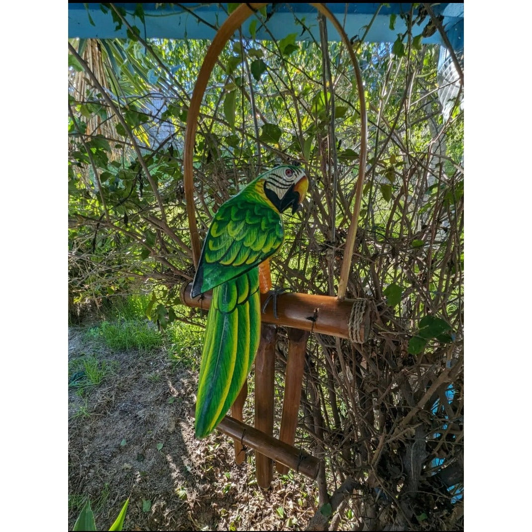 Green macaw parrot perched on a bamboo stand in a garden.