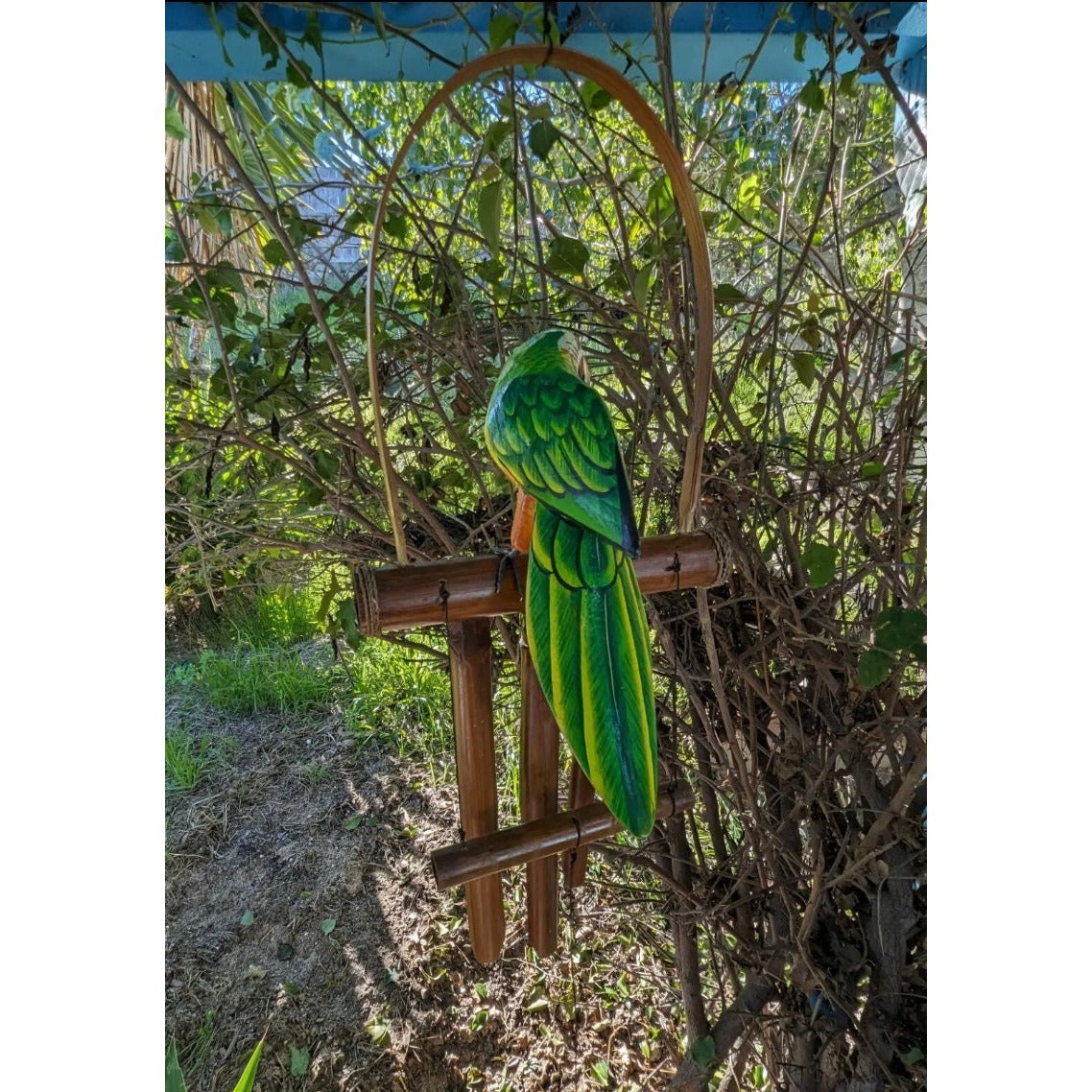 Green parrot sculpture perched on a wooden frame in a garden