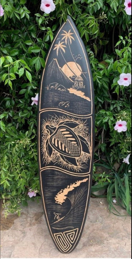 Hand-carved surfboard with tropical motifs: palm trees, mountains, sun, and ocean waves.