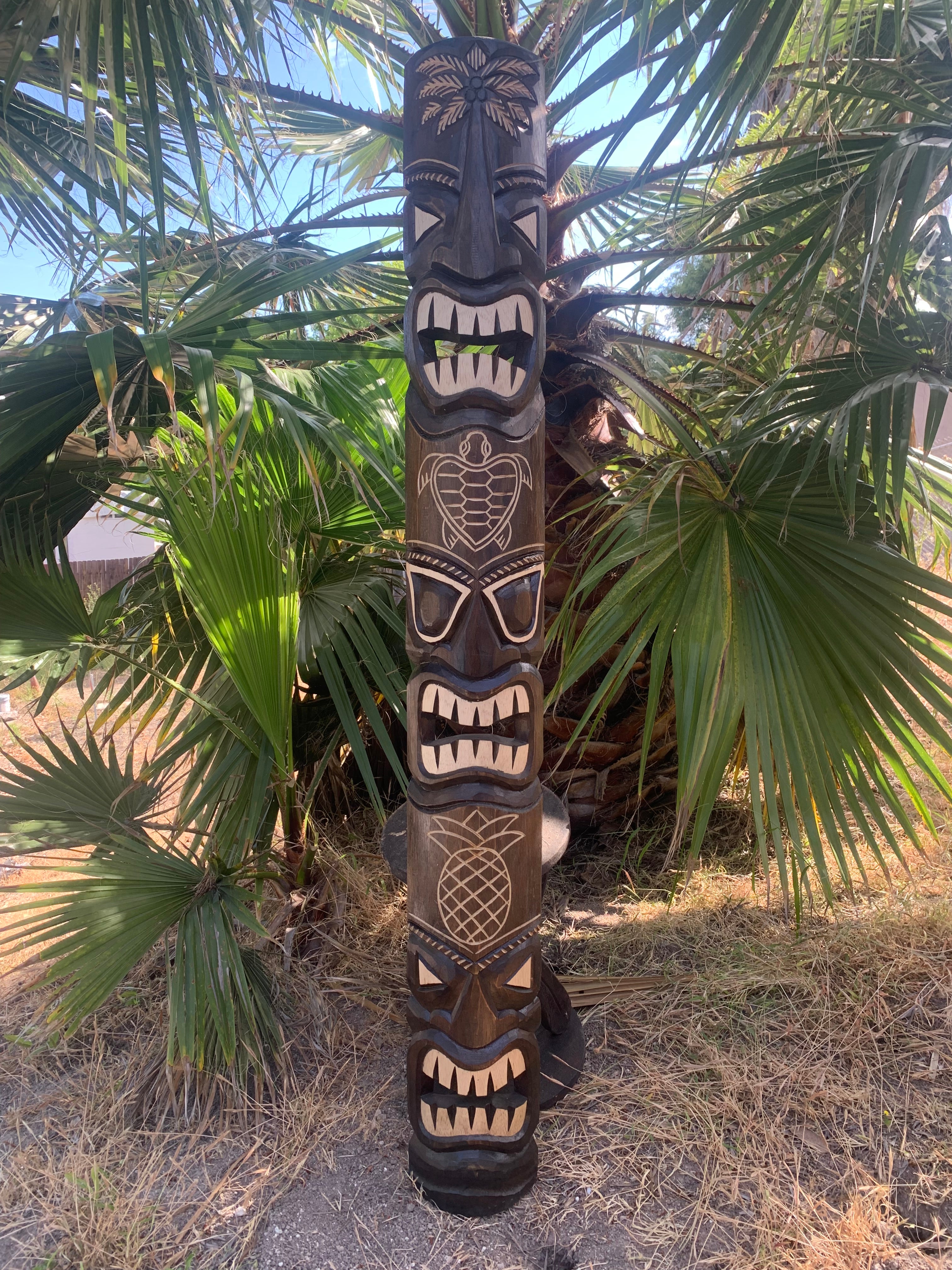 hand-carved tiki totem pole with multiple faces and pineapple motif among palm leaves