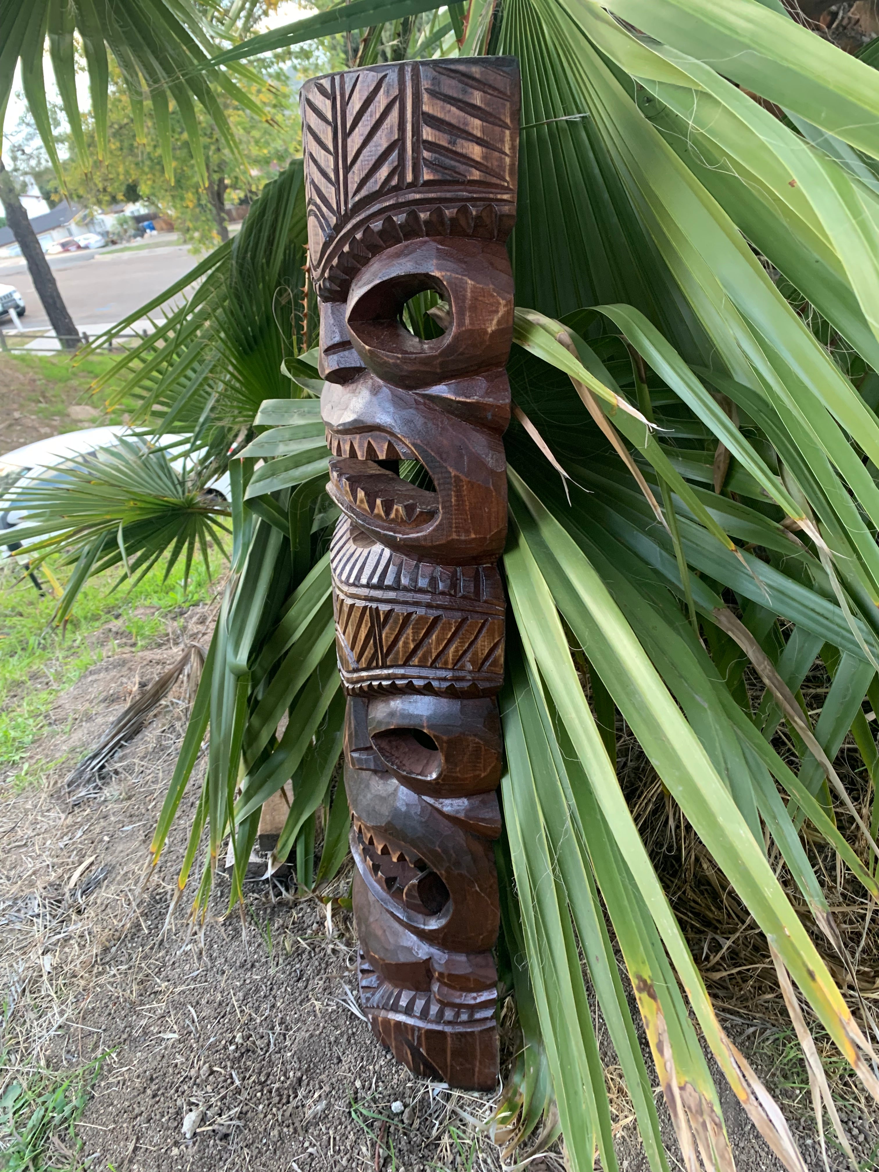Hand-carved wooden tiki totem leaning against palm leaves in a garden