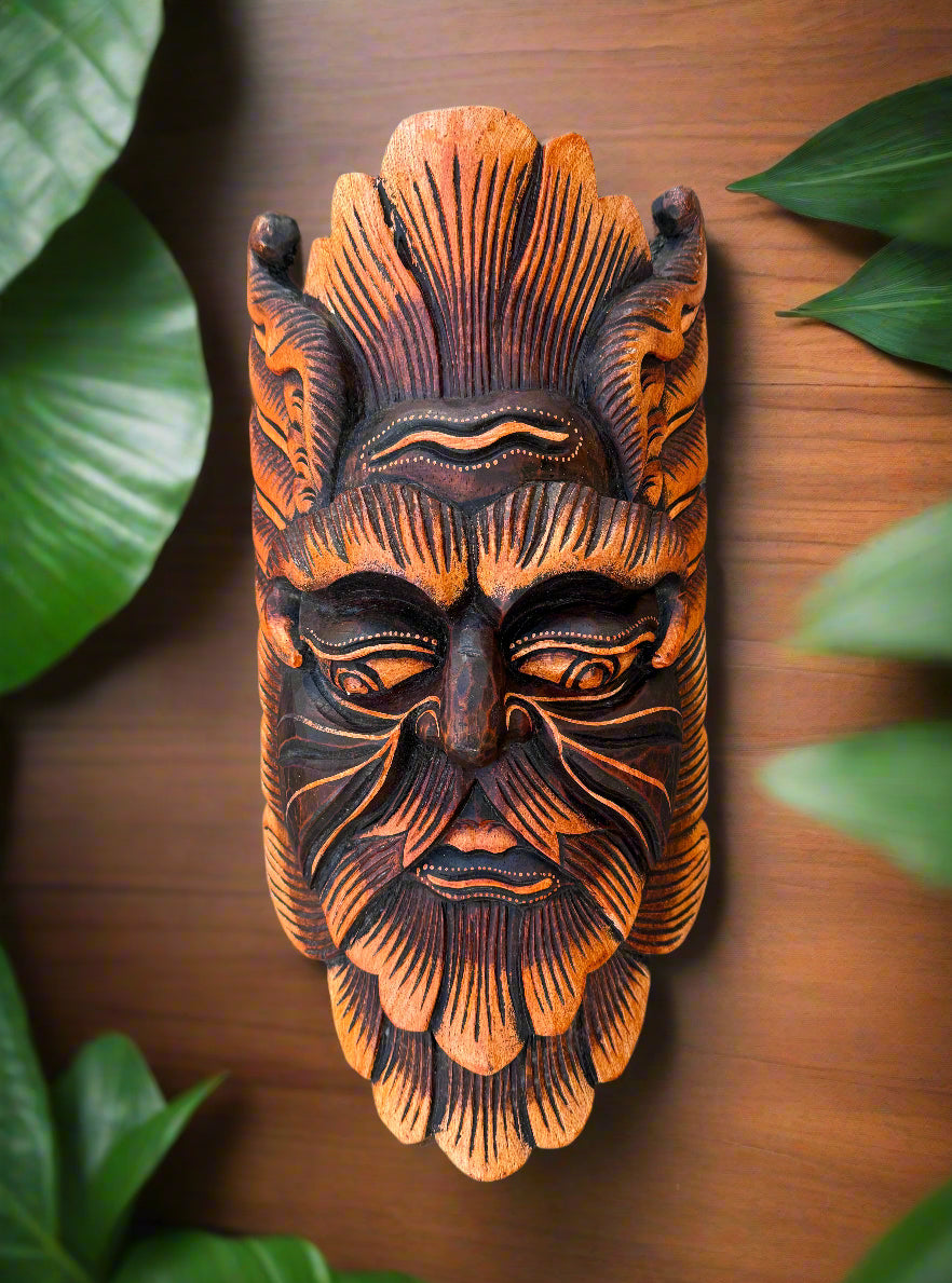 Hand-carved wooden tribal mask with orange and black pattern, framed by green leaves.