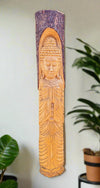 Carved wooden Buddha figure on a vertical panel, wall art with a plant in the background