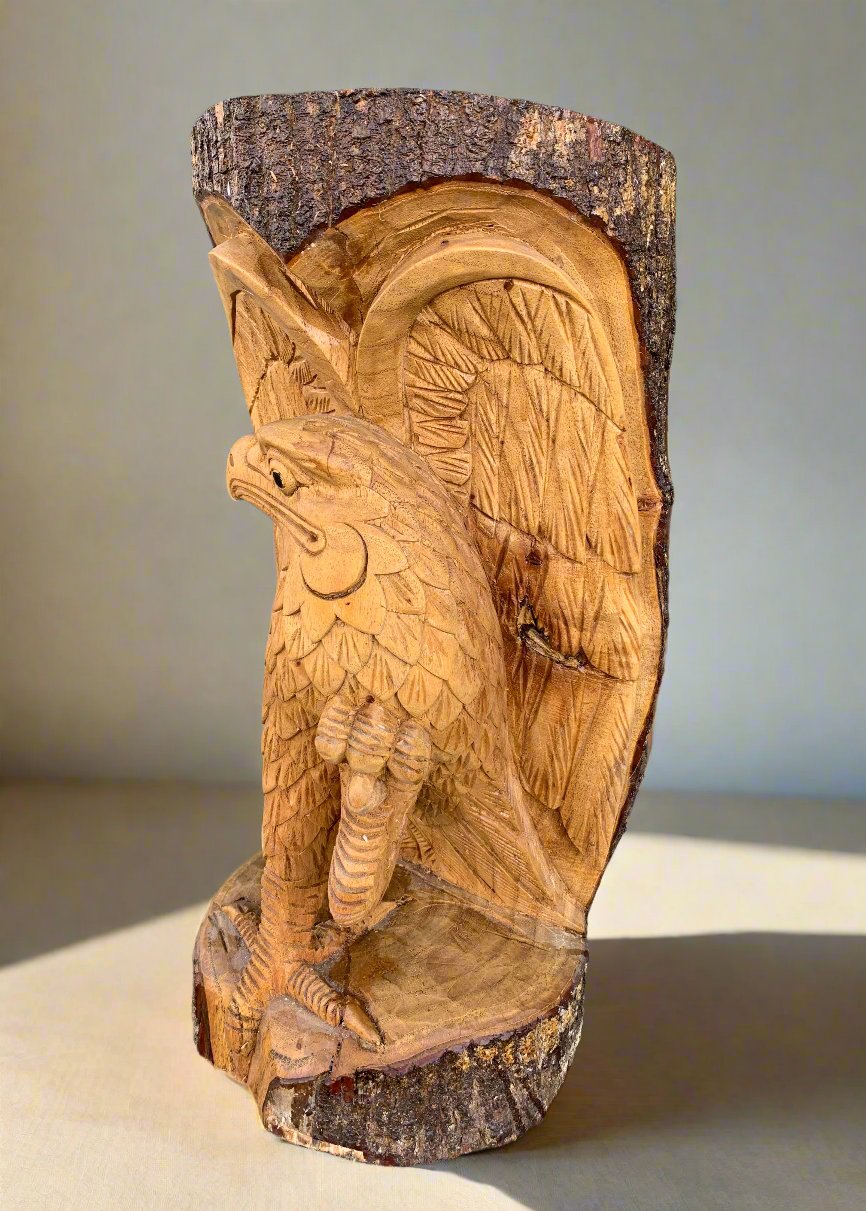 Hand-carved wooden eagle sculpture on a tree trunk with detailed feather textures