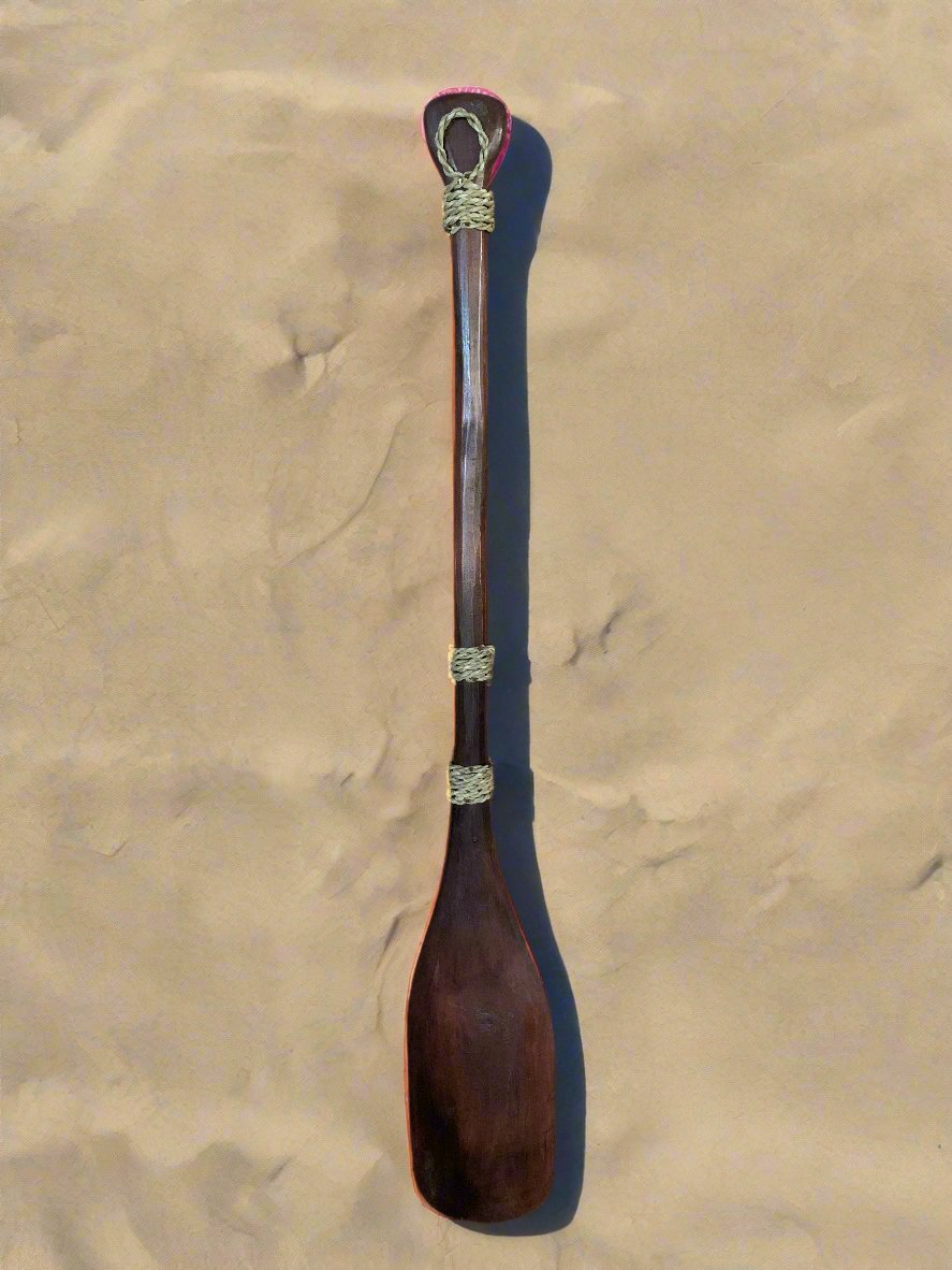 Hand-carved wooden oar with rope bindings on sandy background