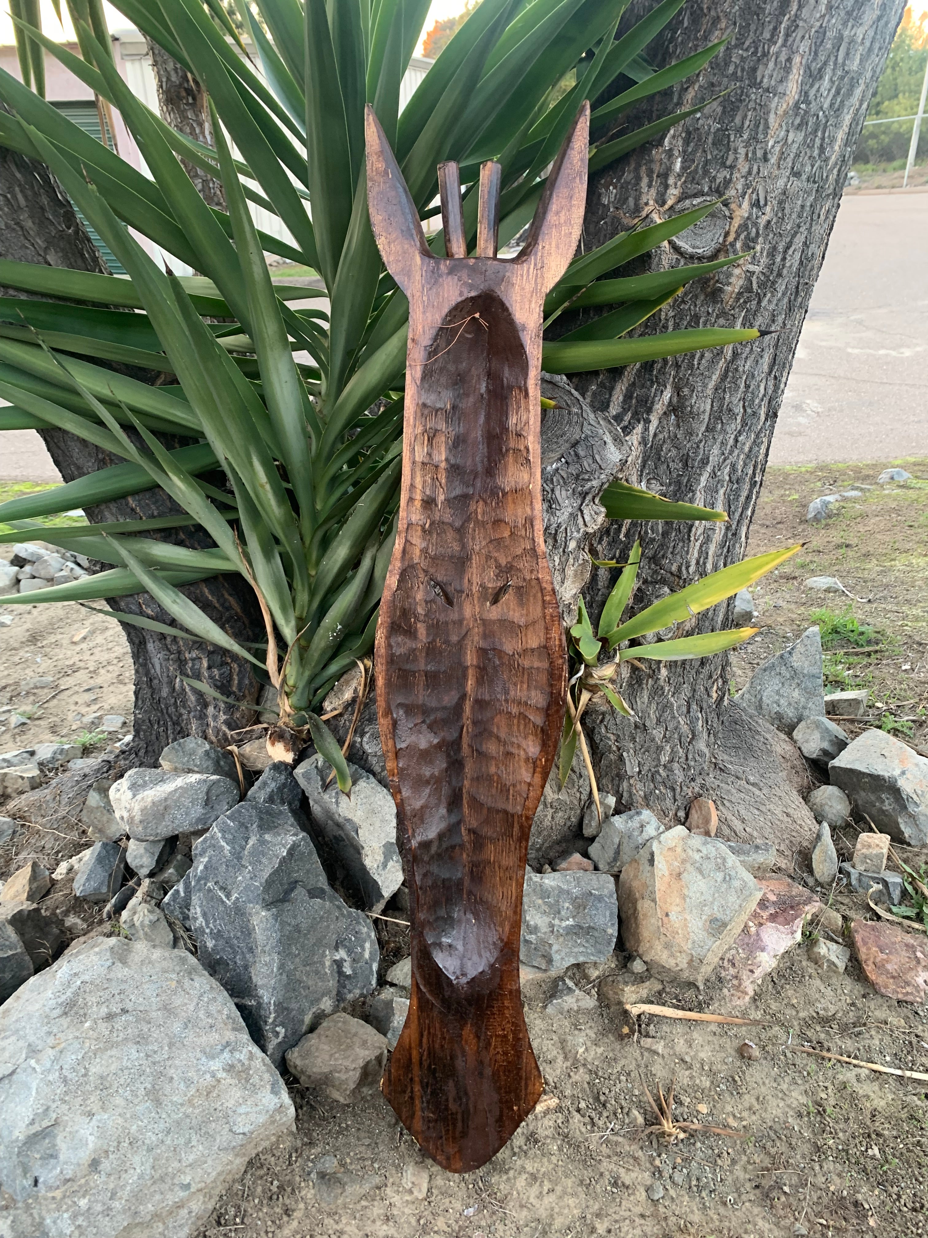 hand-carved wooden paddle sculpture leaning against a tree