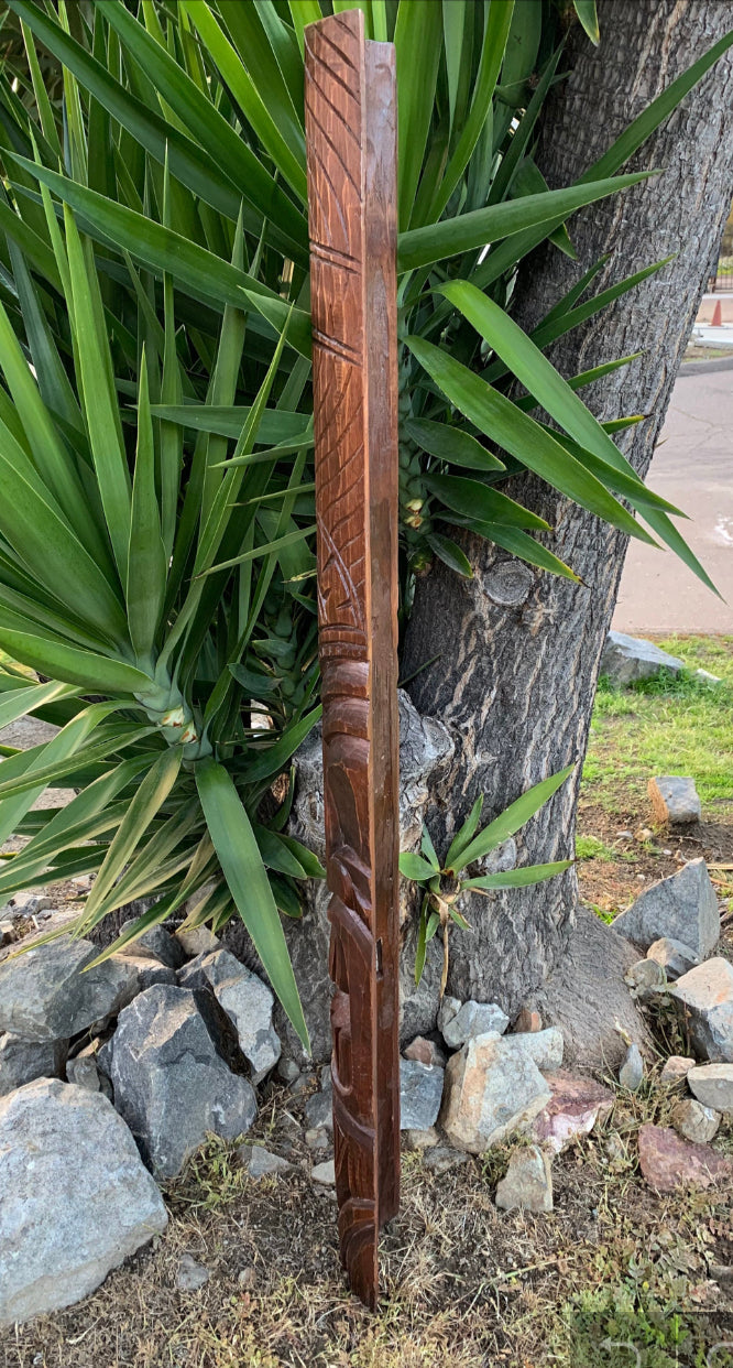 hand-carved wooden post with geometric patterns beside a tree in a garden