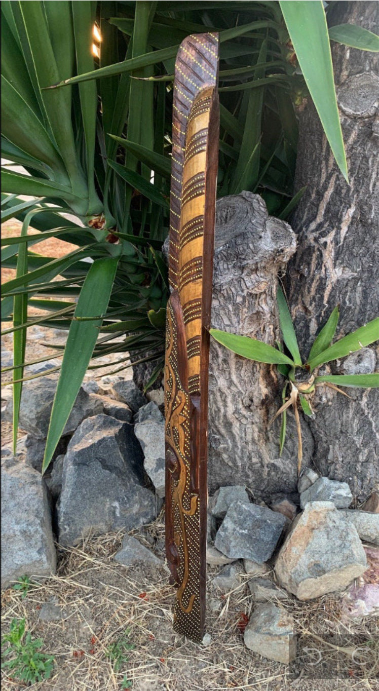 Hand-carved wooden staff with dotted spiral motif leaning against a tree among rocks