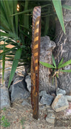Hand-carved wooden staff with dotted spiral motif leaning against a tree among rocks