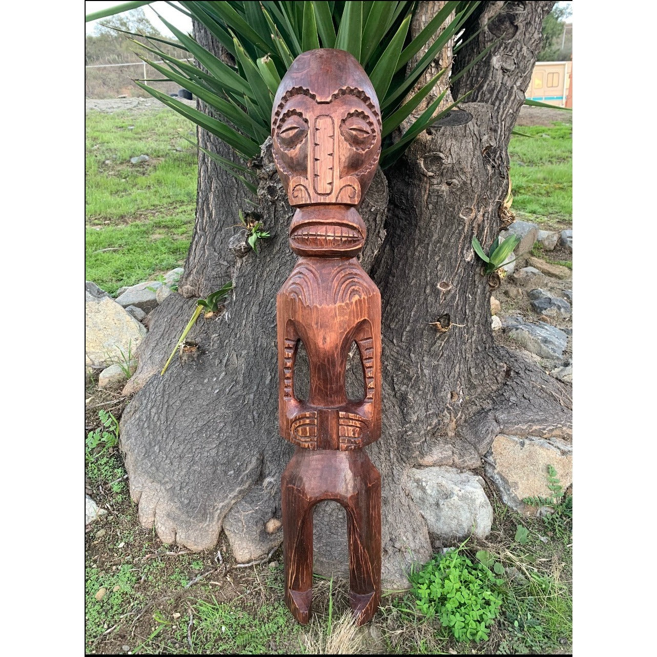 Hand-carved wooden tiki figure leaning against a tree trunk with tribal patterns