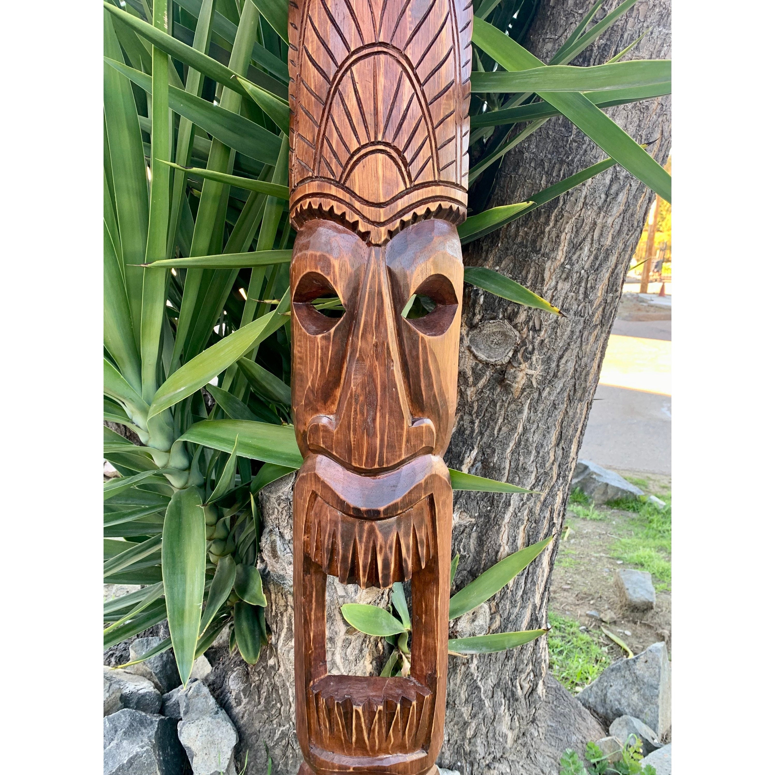 hand-carved wooden tiki mask with hollow eyes hanging on a tree