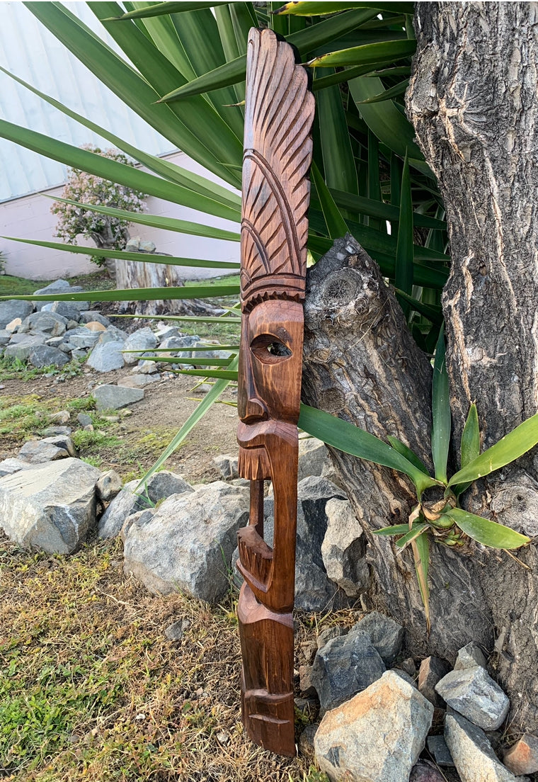 Carved wooden tiki statue leaning against a tree in a garden.
