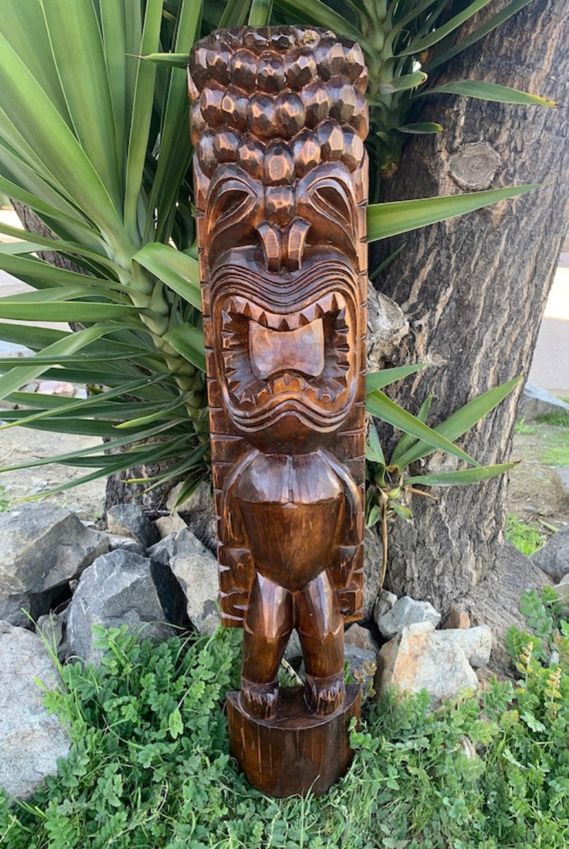 hand-carved wooden tiki statue outdoors amid greenery and rocks