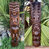 Two tall carved wooden tiki statues with fierce faces in a tropical garden.