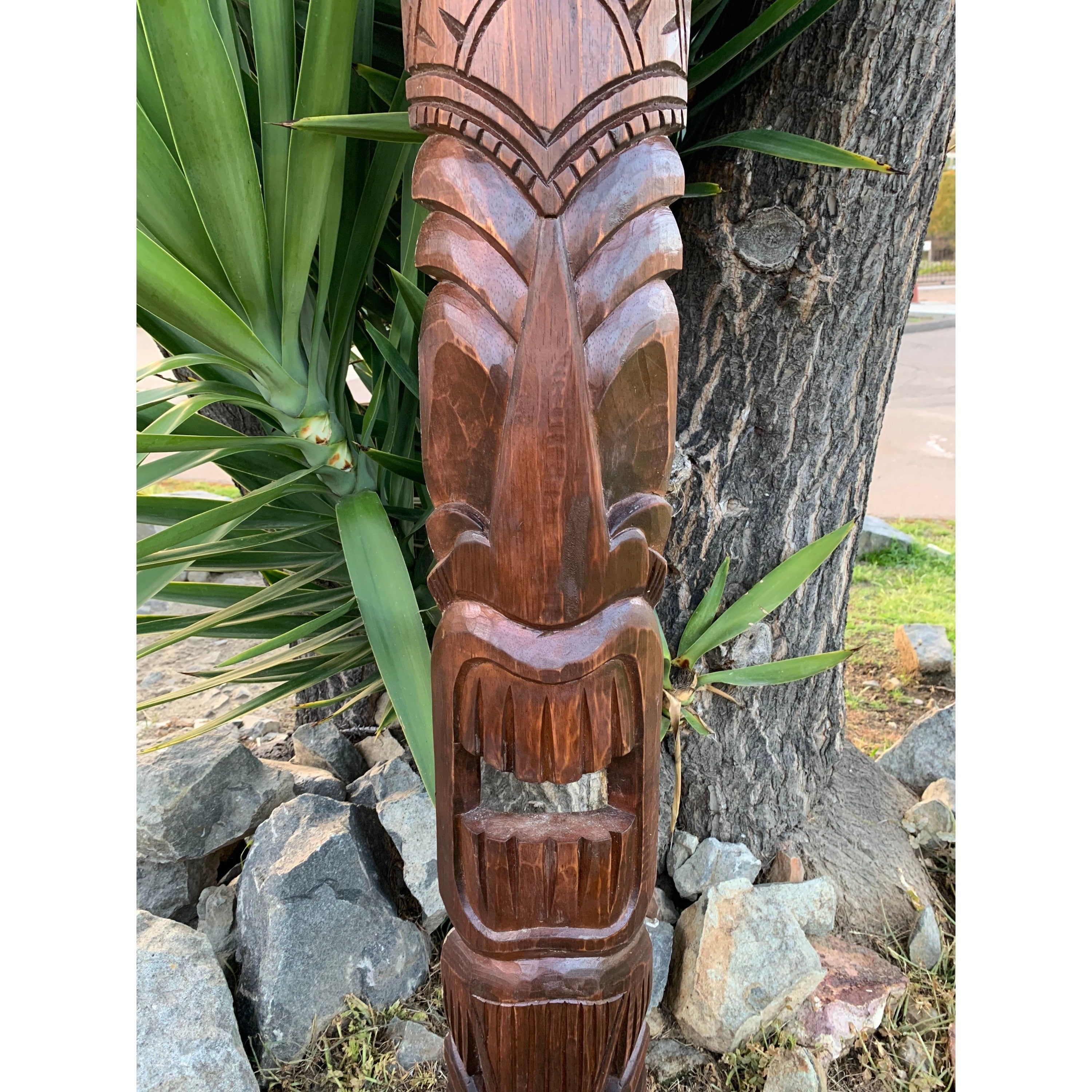 hand-carved wooden tiki totem statue outdoors among rocks and plants