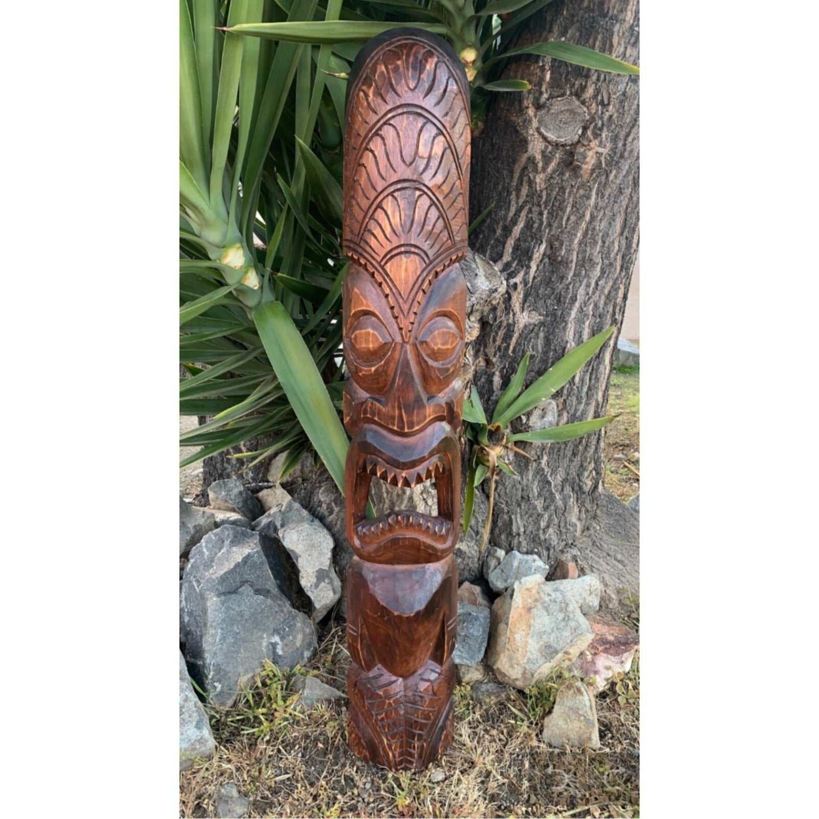 hand-carved wooden tiki totem pole outdoors with a carved face and open mouth