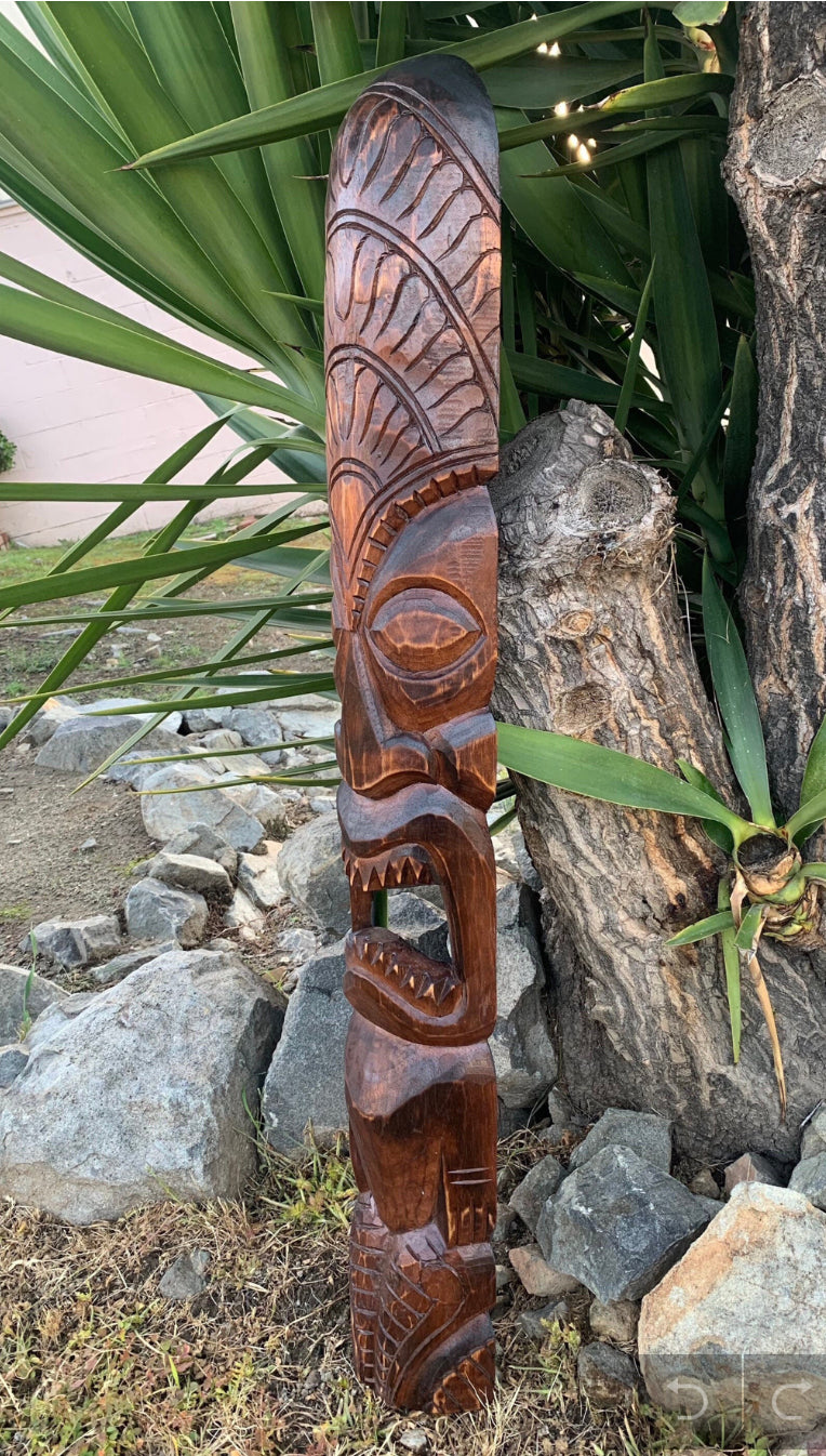 Carved wooden tiki totem pole standing outdoors among rocks and green plants