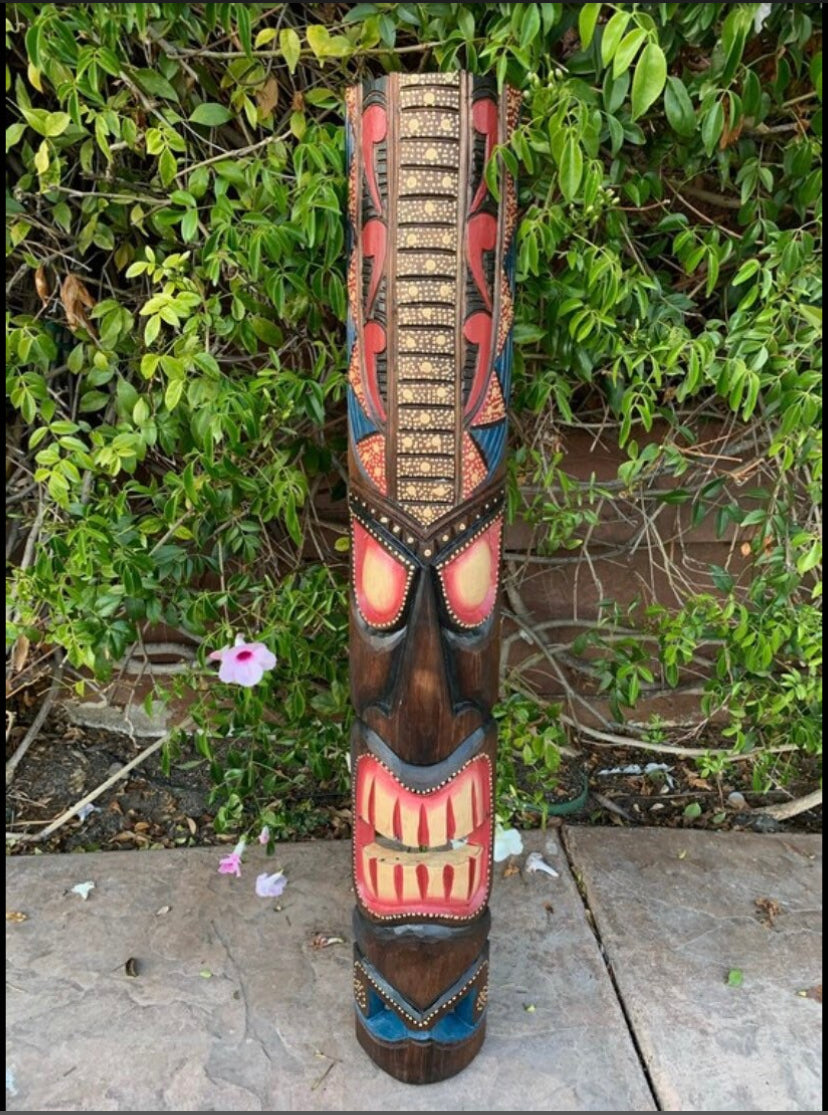 Hand-carved wooden tiki totem pole with colorful geometric patterns outdoors