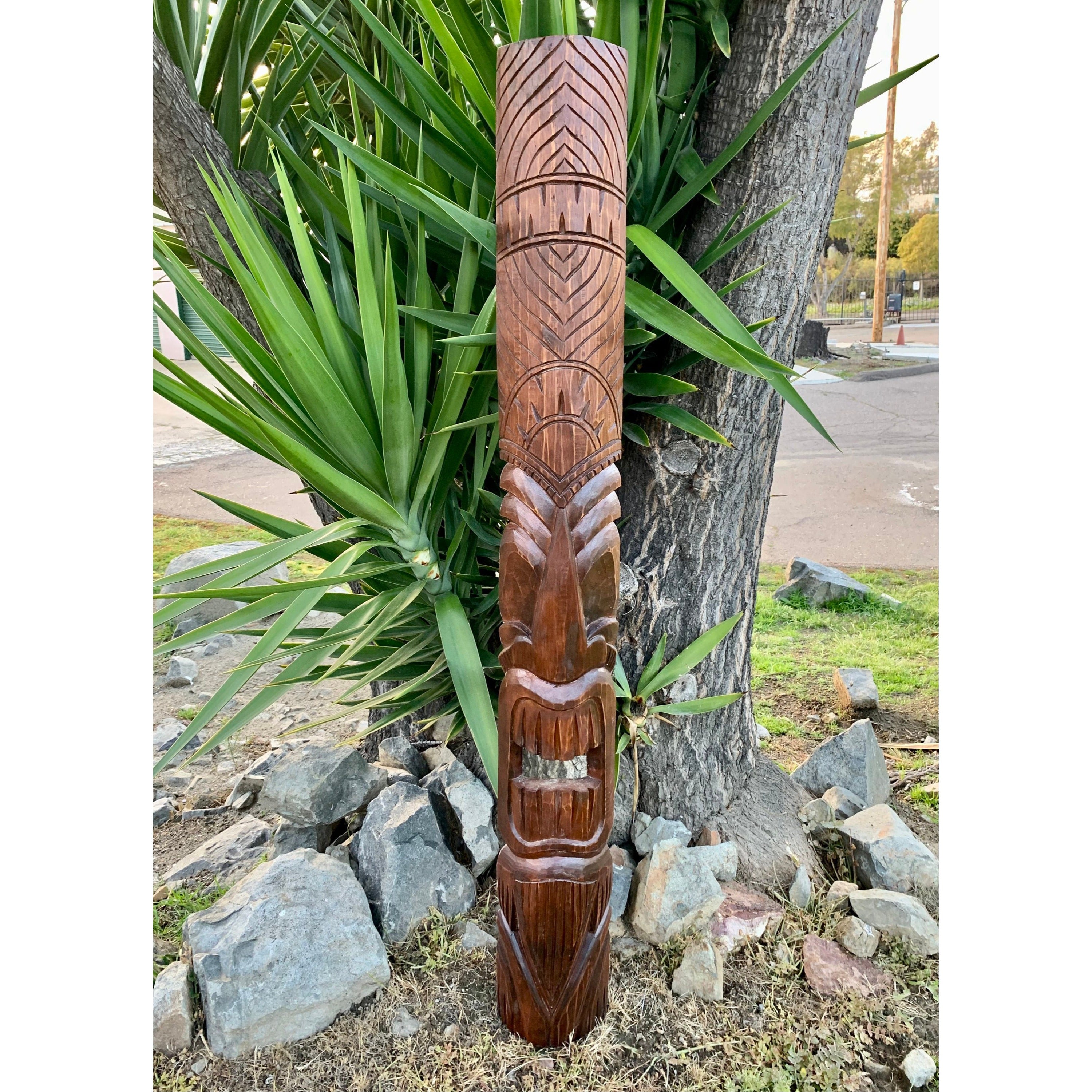 Carved wooden totem pole with geometric patterns outdoors beside a tree.