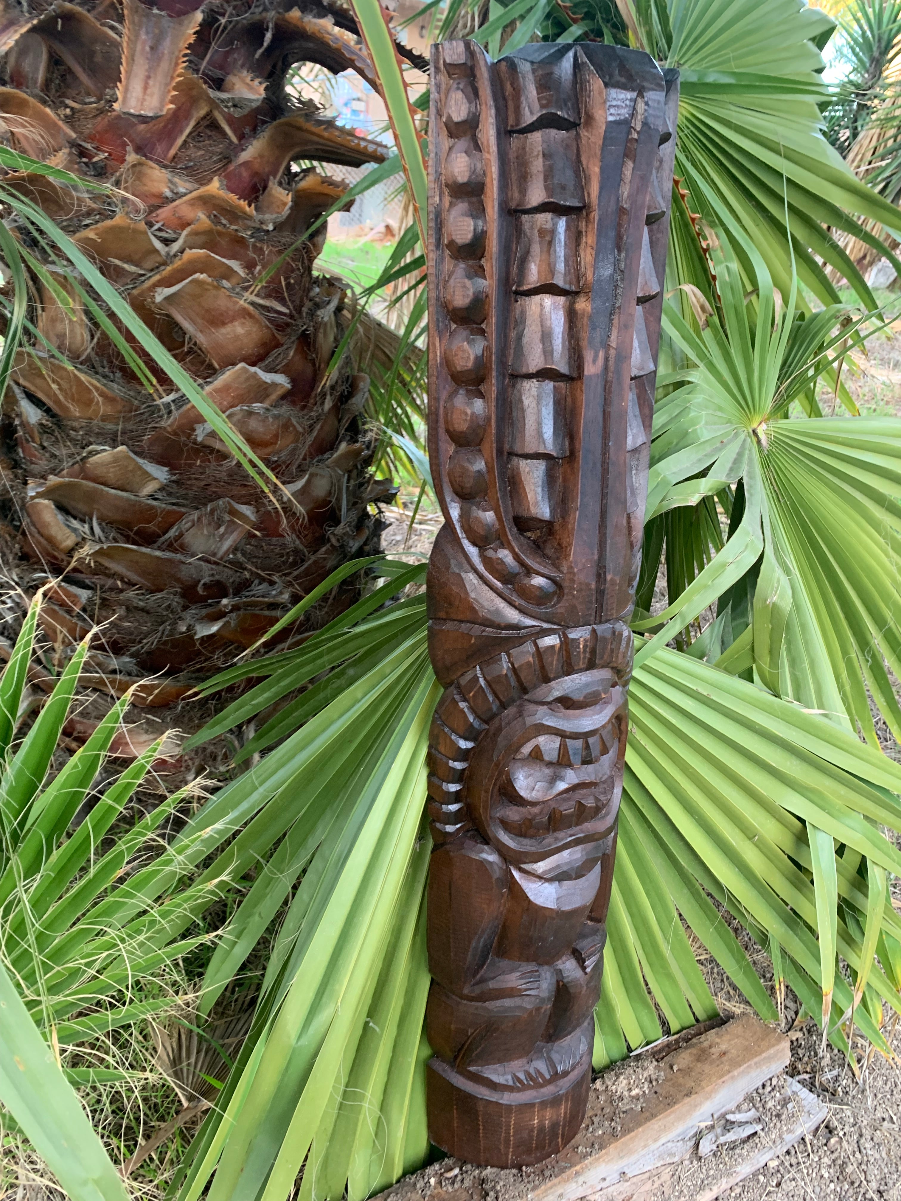 Hand-carved wooden totem pole sculpture amid palm leaves in a garden